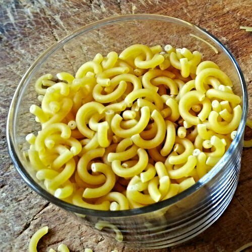 A small glass of fideua pasta sits on a decorative rustic chopping board