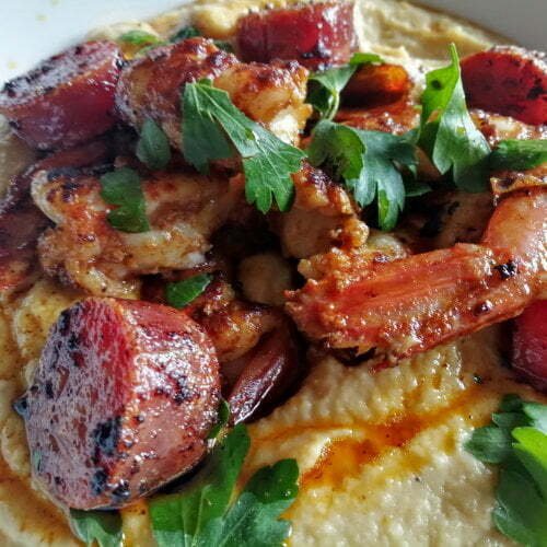 Chorizo, chickpea, and prawn hummus served in an earthenware bowl and garnished with cilantro