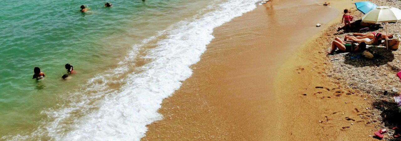 Swimmers enjoy the turquise blue waters of the Mediterranean Sea while other sunbathers bask on the golden sands of the beach