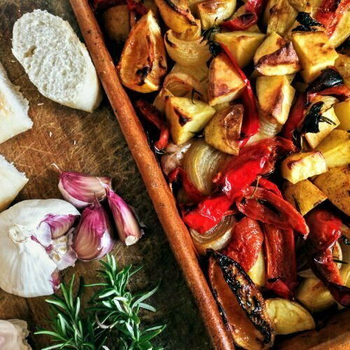 An Earthenware dish of Poor Man's Potatoes sits on a kitchen counter with a chopping board and some bread beside it