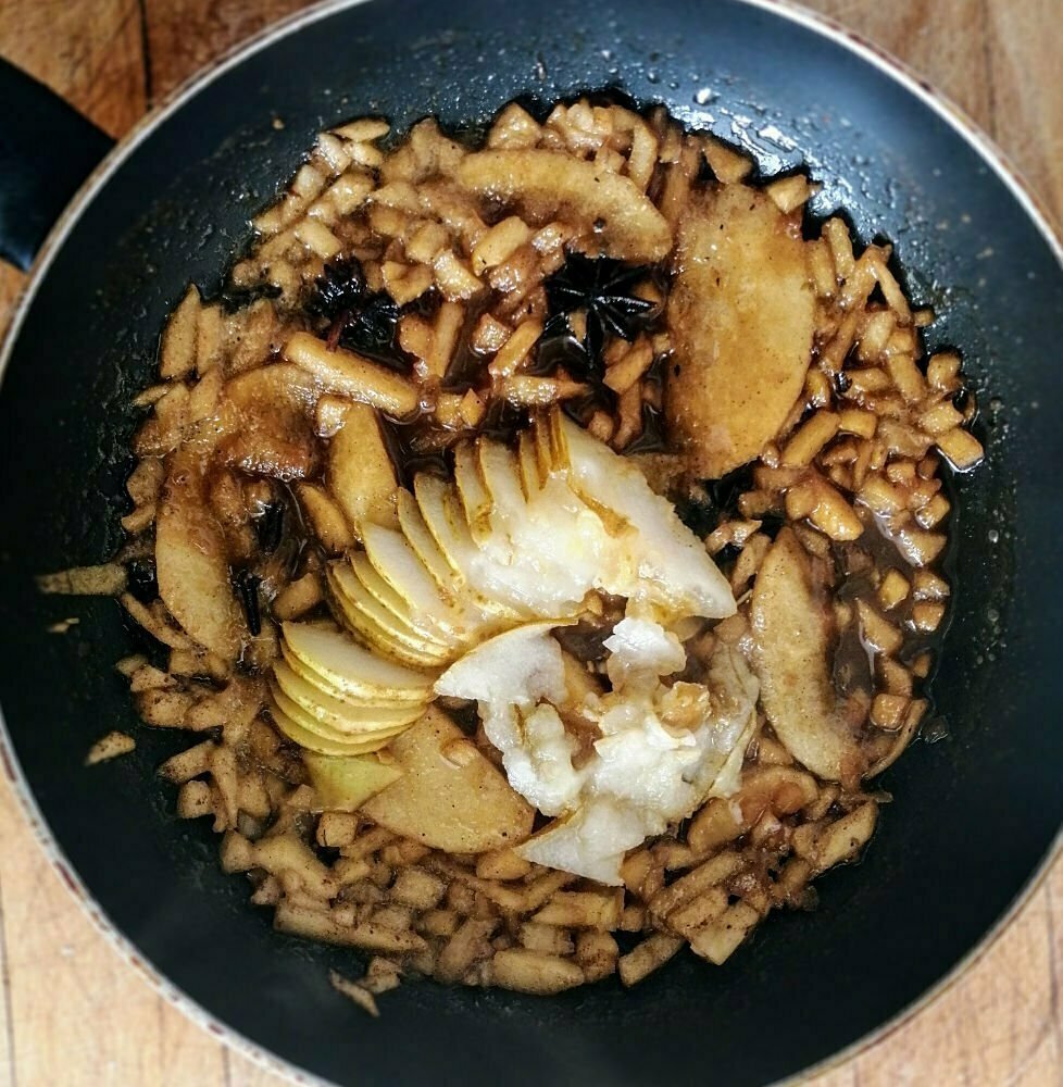 A fryig pan sits with simmering apple and pear slices and a selection of spaices