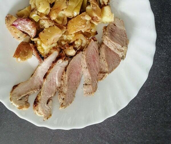 A plate of Spanish pork shoulder slices sits beside some roasted potatoes and garlic