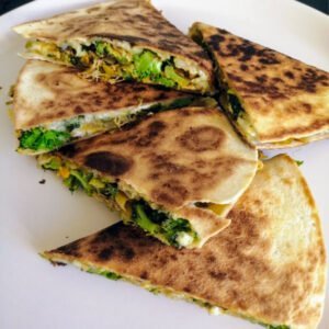 A plate of freshly cooked leek, brocolli, and blue cheese quesadillas sits on a white plate.