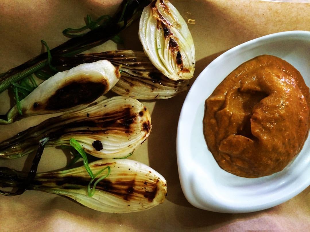 Barbecued calcots sit on a kitchen counter with a side sauce