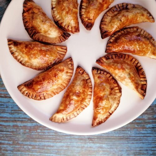 chicken with cider infused chorizo empanadas sits on a white plate on top of a blue wooden benchtop