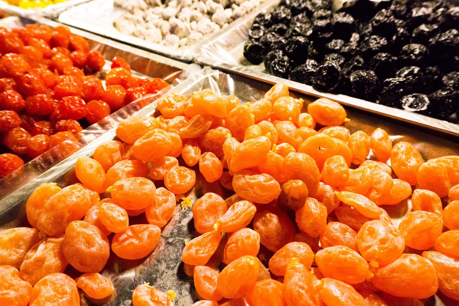 large containers of dried fruits sit at a market stall