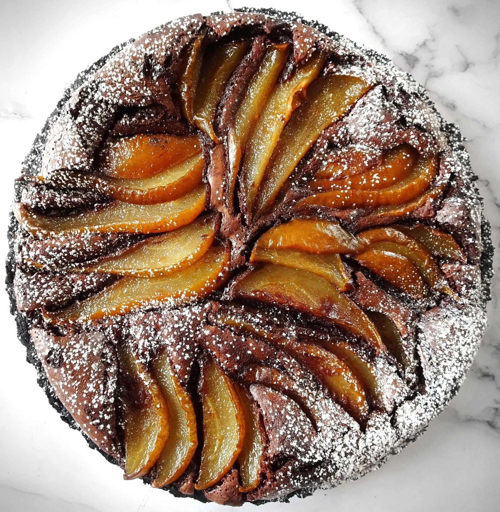 A large Chocolate and pear tart infused in Sweet Spanish sherry sits on a white marble counter