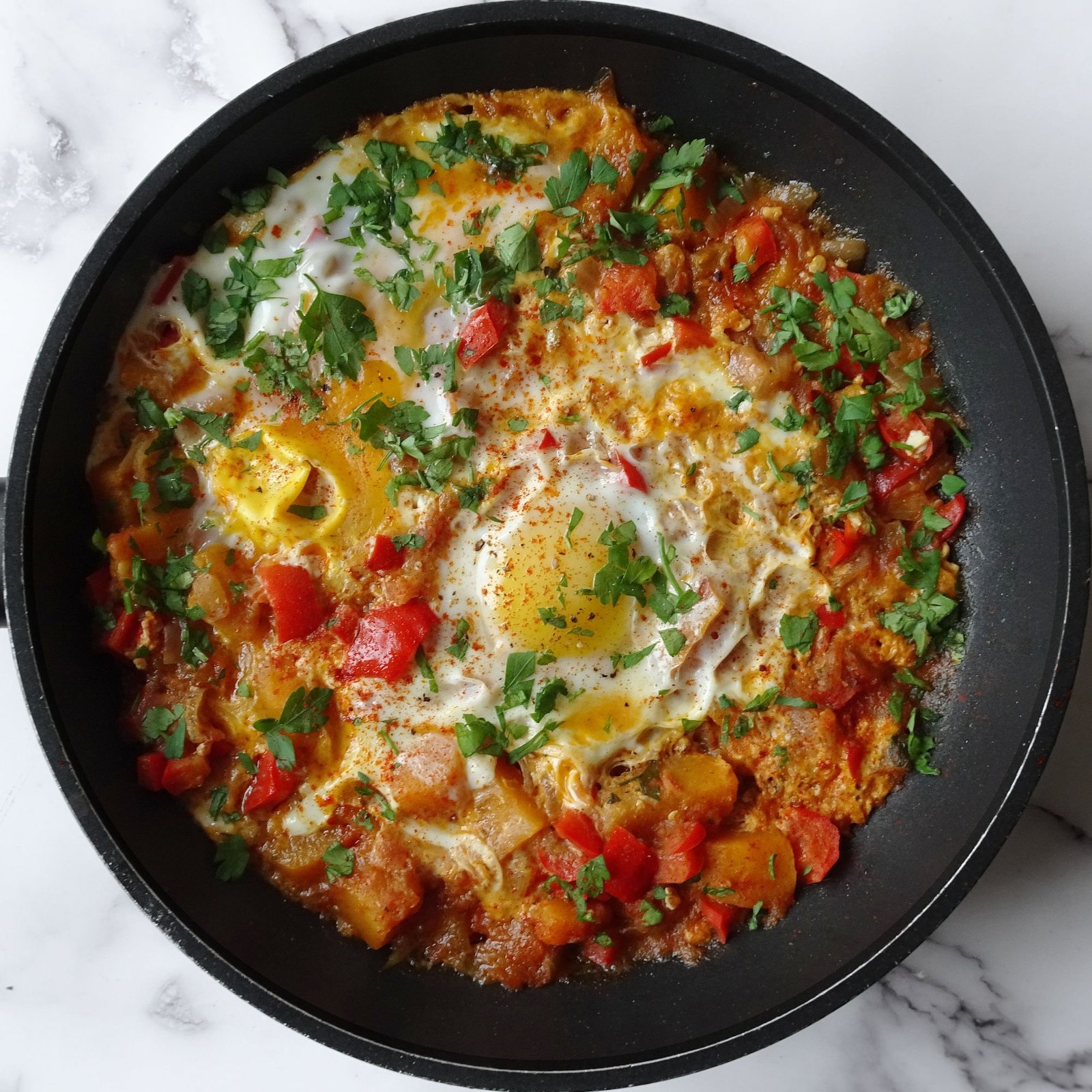 A frying pan of vegetable pisto with eggs with some parsley garnish on top