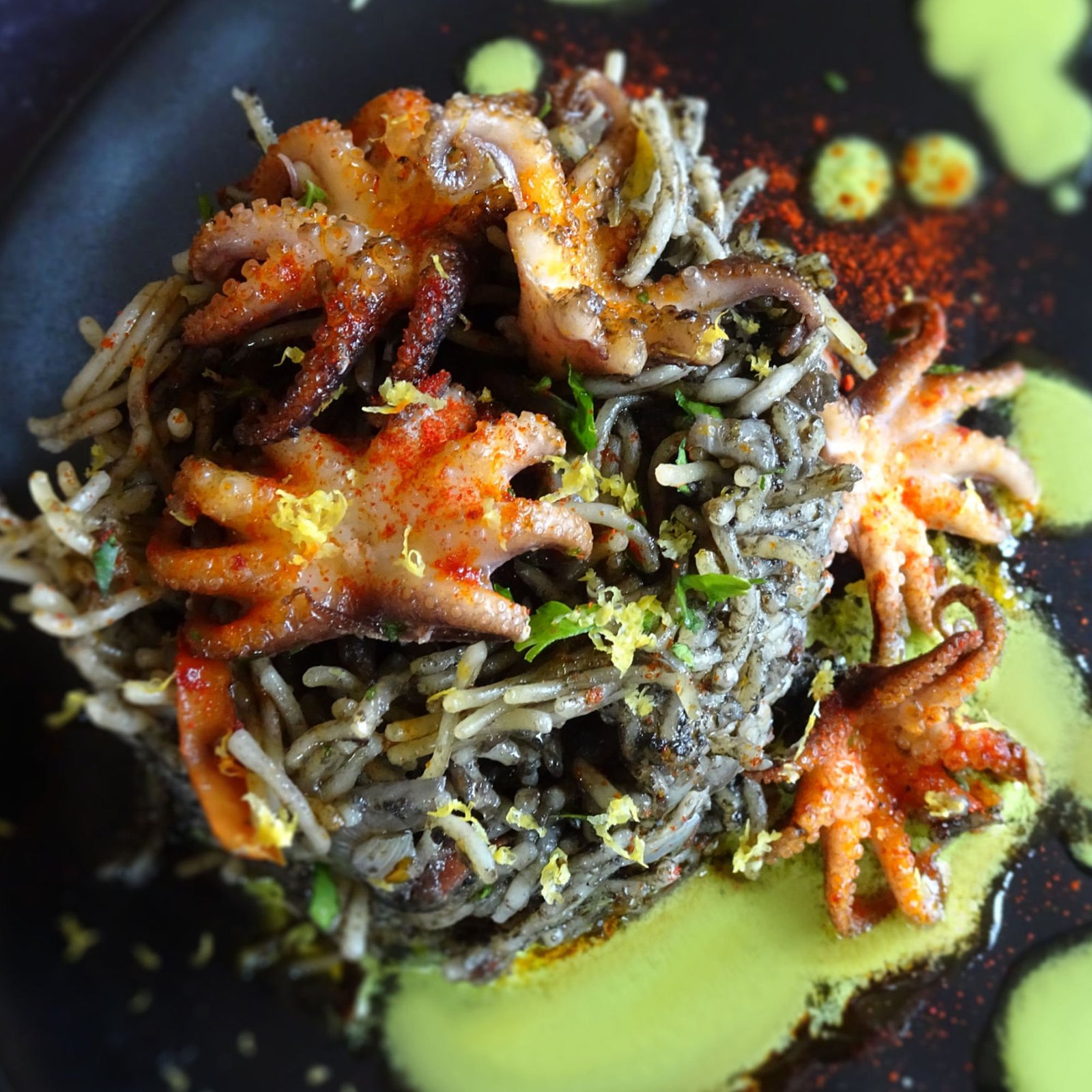 A close up shot of a tower of fideua pasta that is stained with squid ink and topped with baby squid