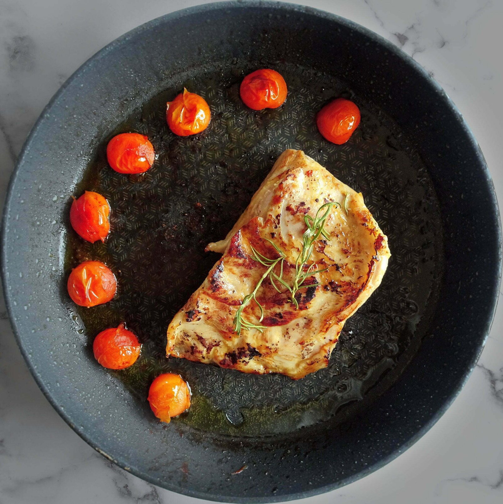 a cerdo secreto fillet sits in a frying pan dotted with fried cherry tomatoes