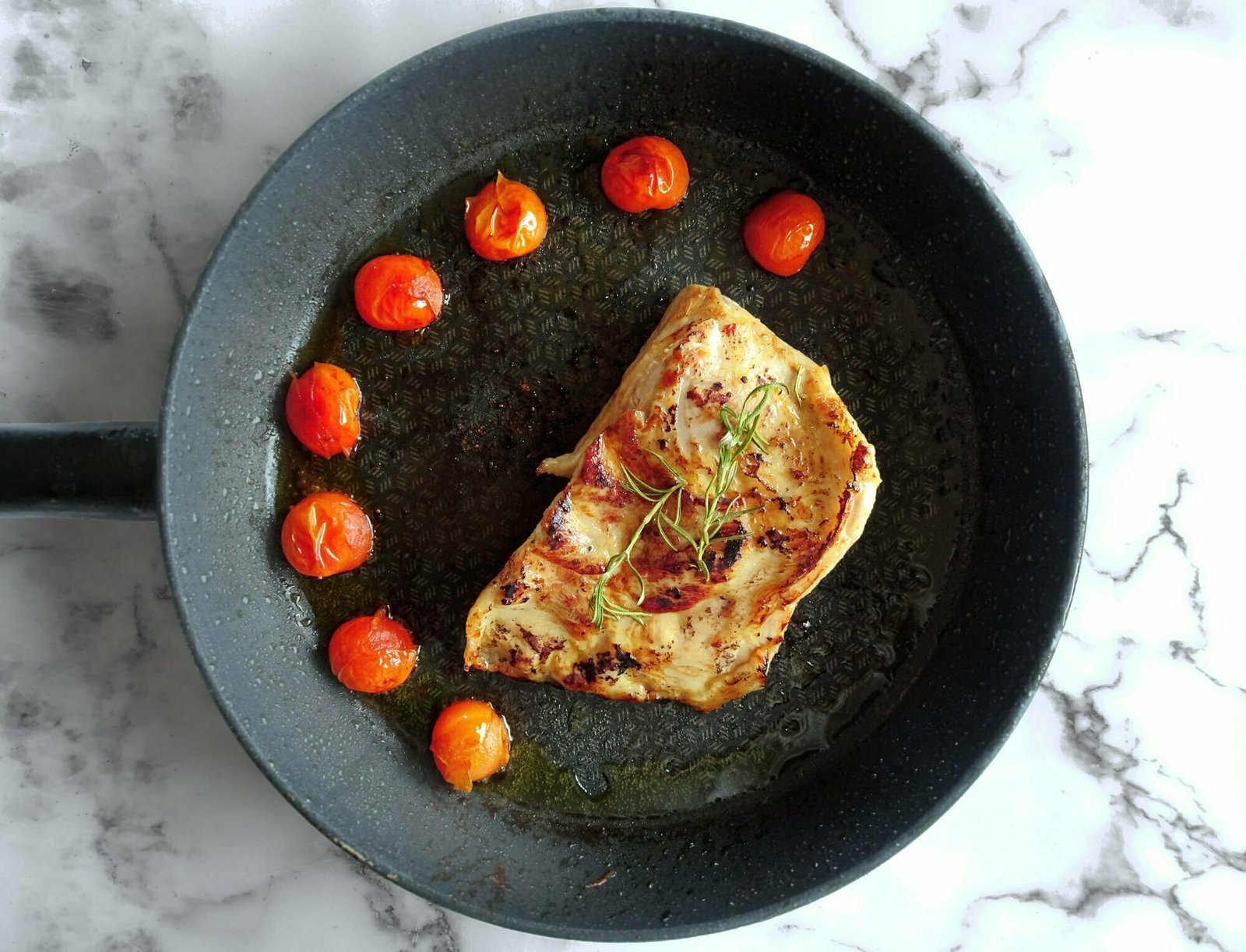 a cerdo secreto fillet sits in a frying pan dotted with fried cherry tomatoes