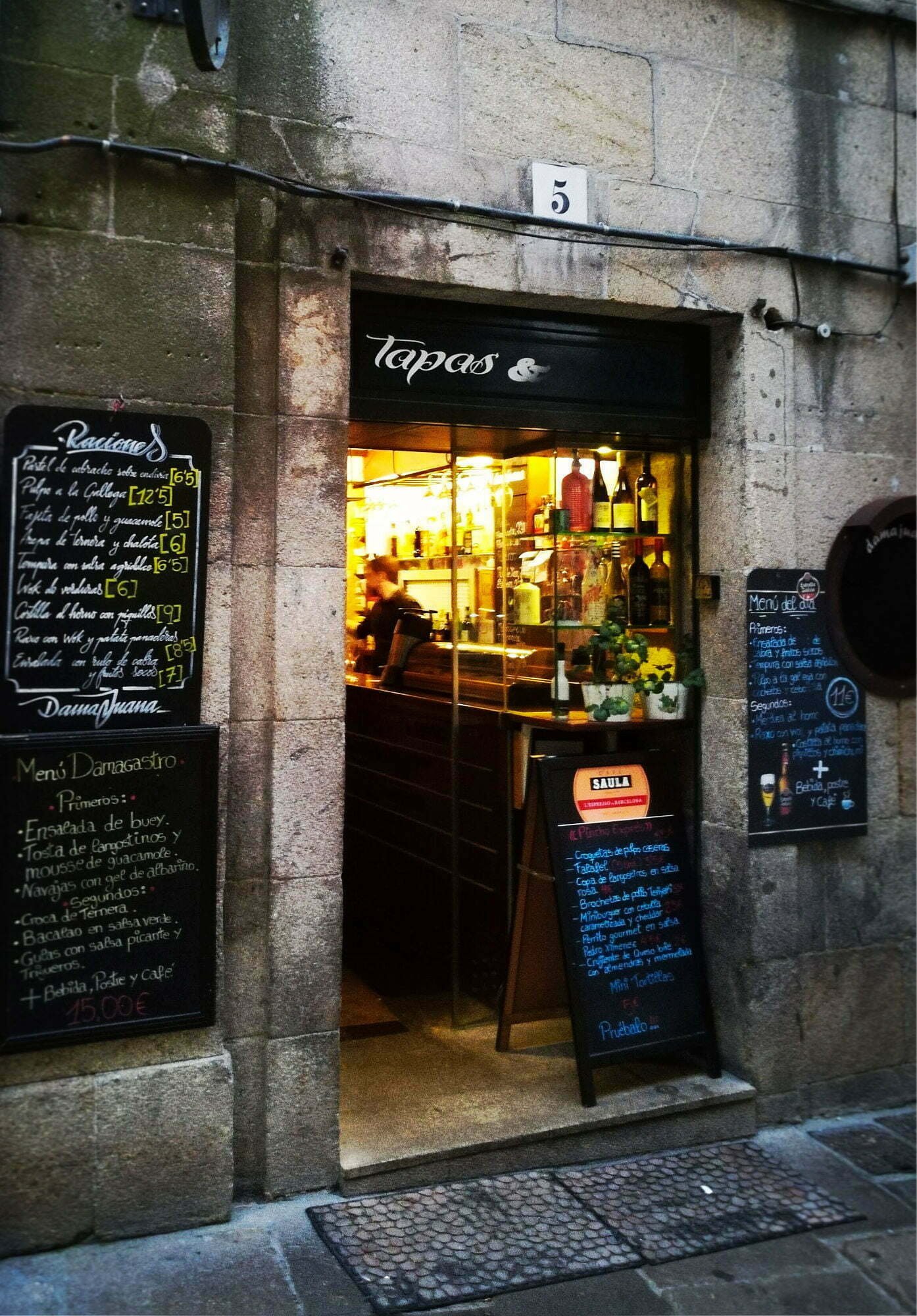 a tapas bar in the heart of Santiago de Campostella opens its front door where a soft yellow light illuminates the many tapas dishes on display inside.