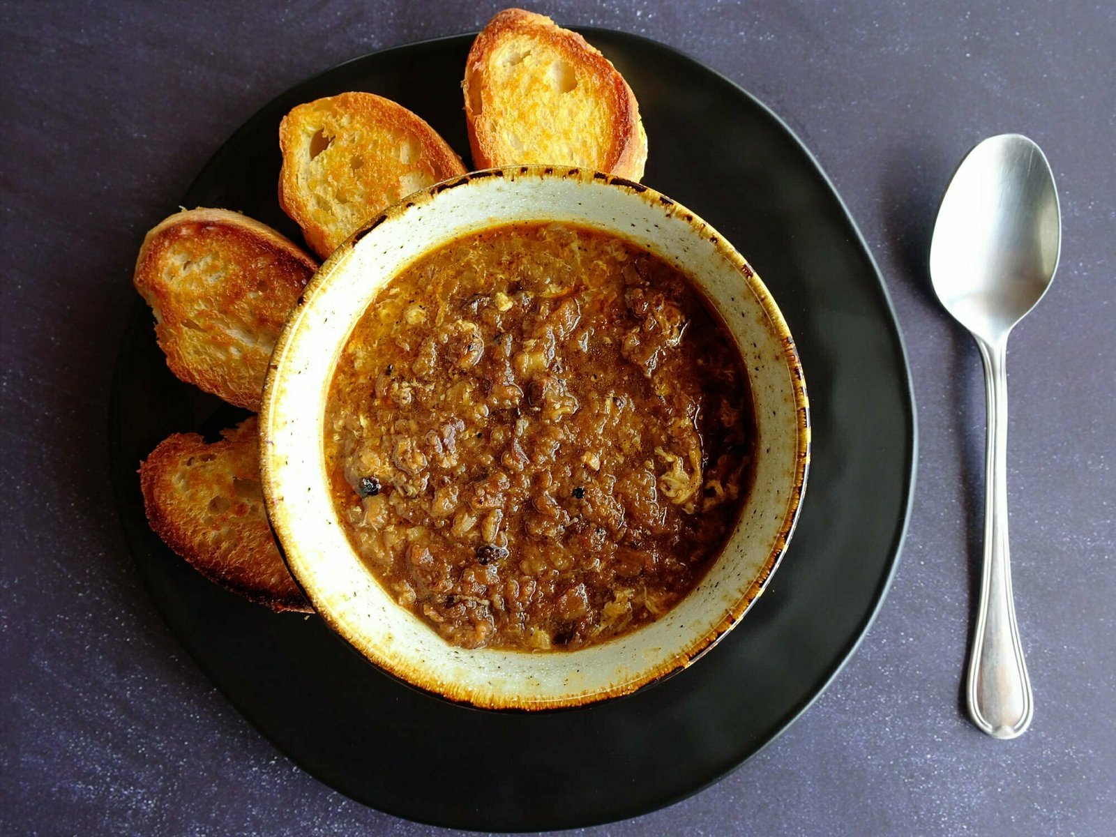 garlic soup sits in an ornamental white bowl beside a few slices of golden toasted bread