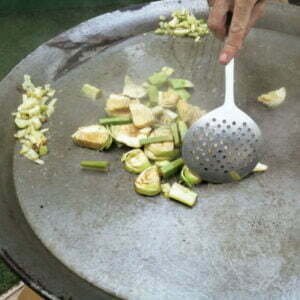 A large paella pan is frying some onion, garlic, artichoke pieces, and pepper.