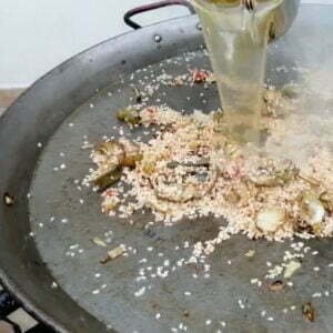 Adding vegetable broth to the paella pan and ingredients