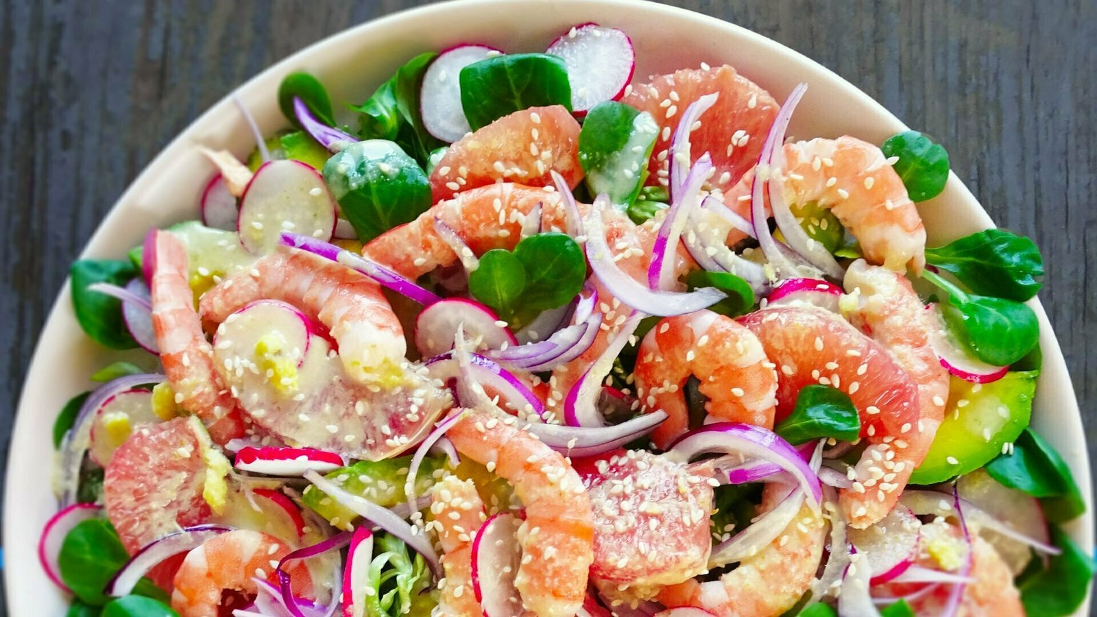 A round plate sit on a wooden counter full of color shrimp avocado salad