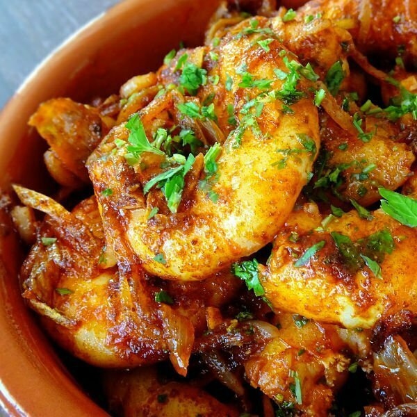 close up shot of sizzling garlic shrimp in a earthenweare dish topped with some fresh chopped parsley