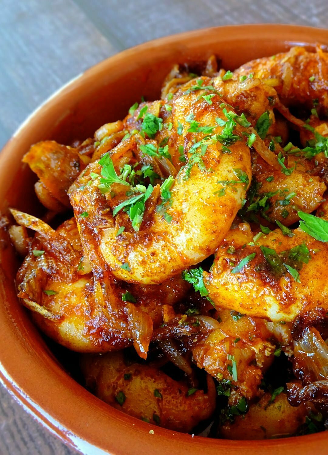 close up shot of an earthenware dish filled with gambas al ajillo (garlic prawns) and topped with some chopped parsley