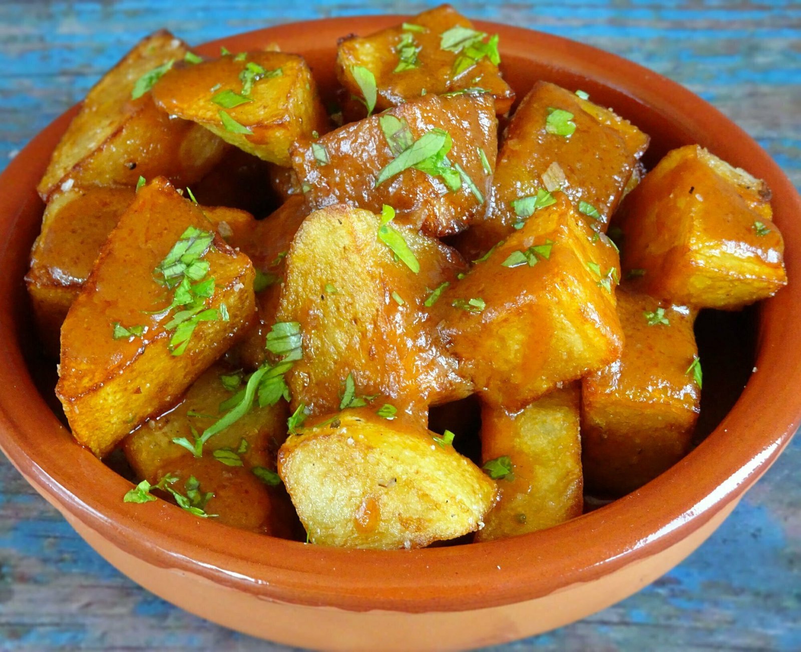 A erthen eare dish sits on a rustic wooden board with some patatas bravas