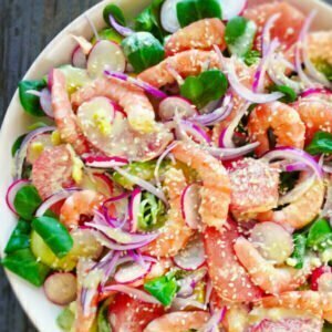 A colorful shrimp and avocado salad sits on a white plate with bright red radishes, pink grapefruit, red onion, and cooked shrimp