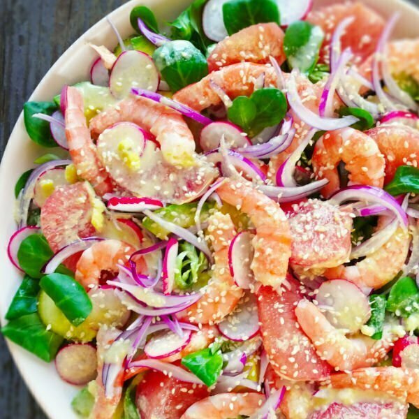 A colorful shrimp and avocado salad sits on a white plate with bright red radishes, pink grapefruit, red onion, and cooked shrimp