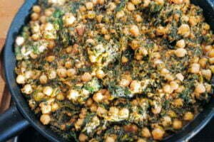 A large pan of spinach with chickpeas sits cooking on a stovetop