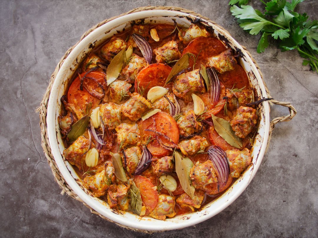 oven baked fish casserole sits on a grey granite kitchen worktop beside some fresh sprigs of parsley. 