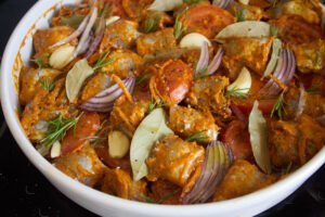 A tray of fish is marinated in romesco sauce and garnished with. rosemary and bay leaves.