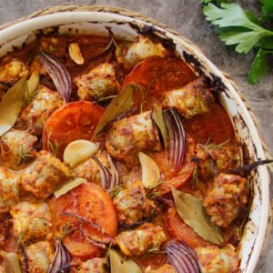 A large casserole dish sits with fish, tomato, red onion, and romesco sauce