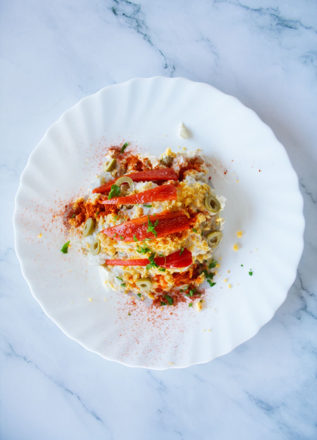 a plate of ensalada rusa is garnished with a few strips of roasted pepper and some egg yolk