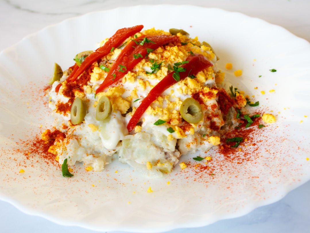 a plate of ensalada rusa is garnished with a few strips of roasted pepper and some egg yolk