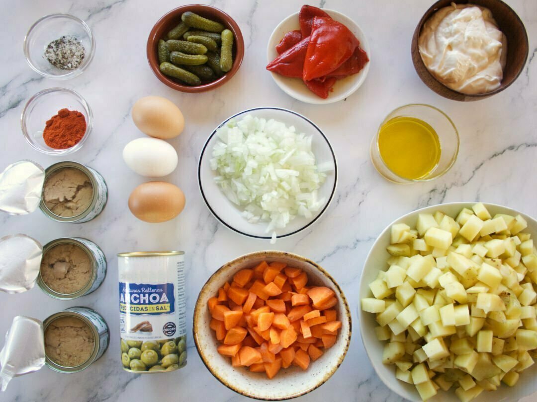 ingredients used to make ensalada rusa are laid out on a white marble benchtop