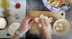 two hands peel hard boiled eggs bbeside some prepared ingredients for ensalada rusa