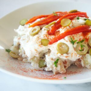 a plate of ensalada rusa is garnished with a few strips of roasted pepper