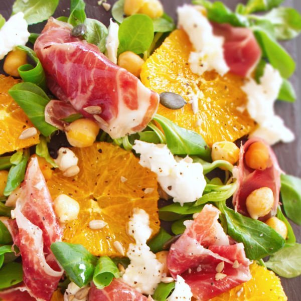 A large platter of jamon iberico sald sits topped with mozarella, salad greens, chickpeas, and seasoned with salt and pepper