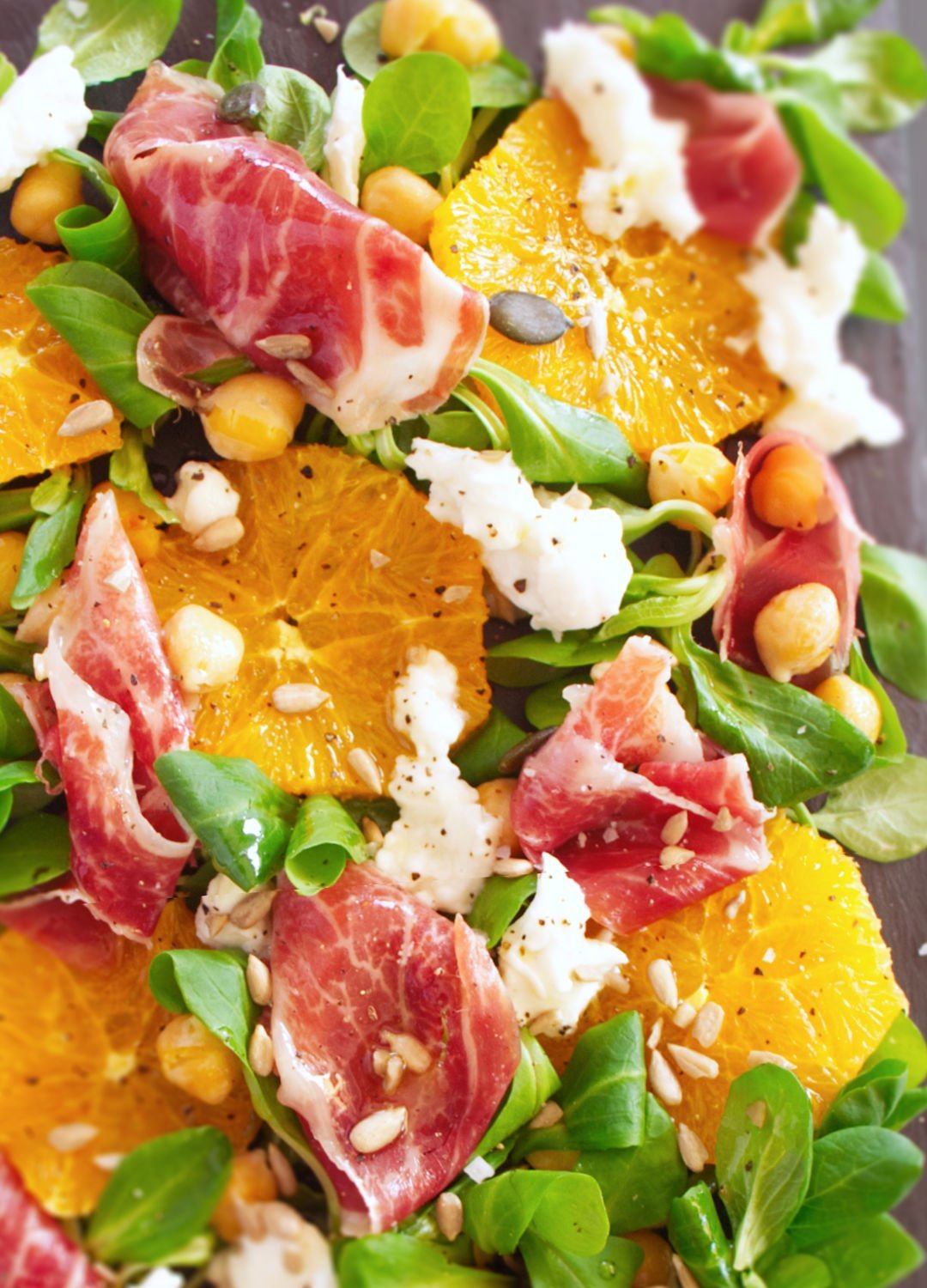 A large platter of jamon iberico sald sits topped with mozarella, salad greens, chickpeas, and seasoned with salt and pepper