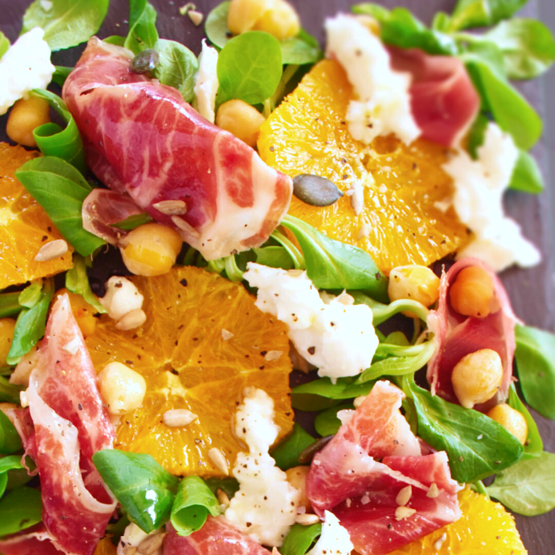 A large platter of jamon iberico sald sits topped with mozarella, salad greens, chickpeas, and seasoned with salt and pepper