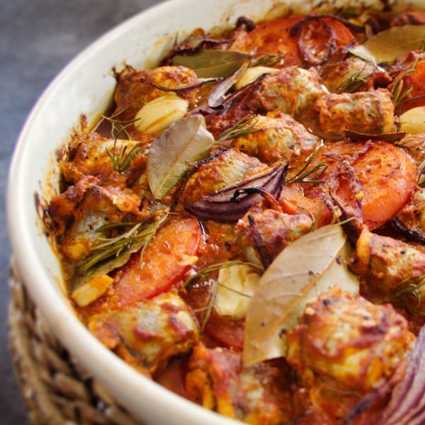 oven baked fish casserole sits on a grey granite kitchen worktop beside some fresh sprigs of parsley.