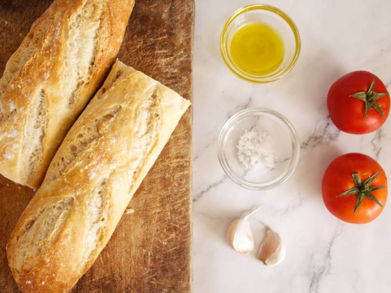 ingredients used to make pan con tomate are laid out on a white marble counter top 