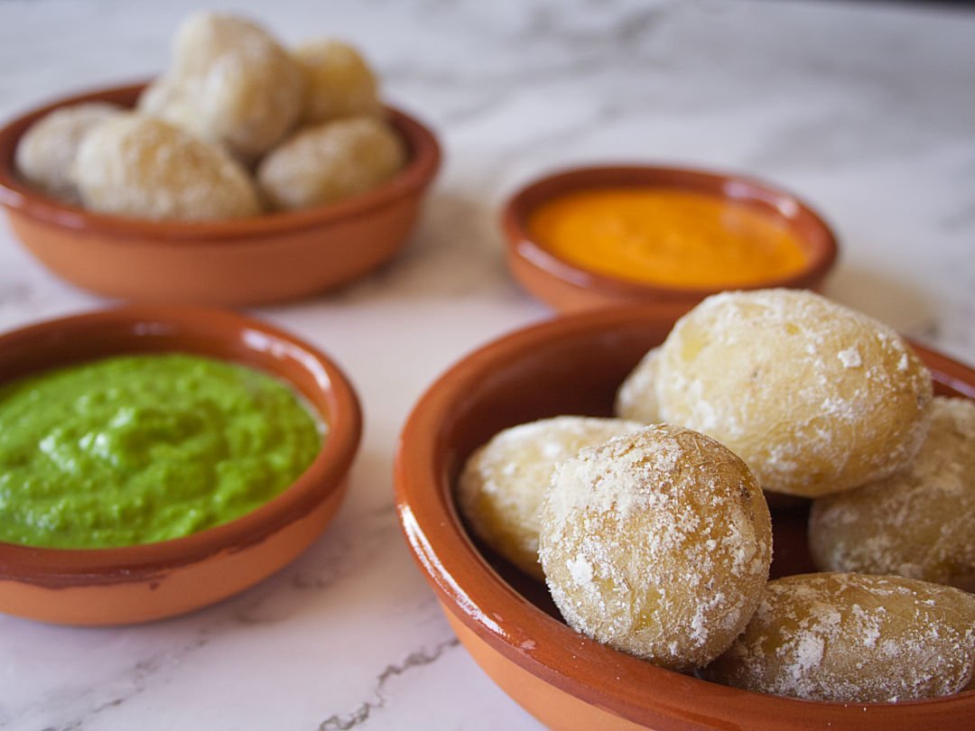 Small earthenware dishes filled with papas arrugadas, green mojo, and red mojo sauces.