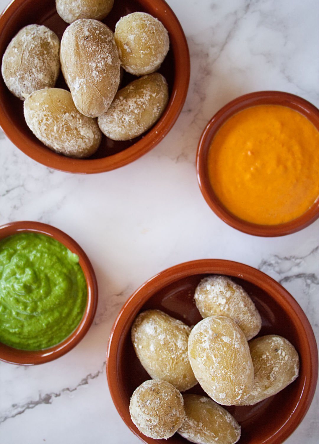 Small earthenware dishes filled with papas arrugadas, green mojo, and red mojo sauces.