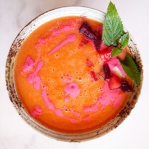 A small ceramic bowl sits filled with water melon gazpacho that has been garnished with a few sprigs of mint