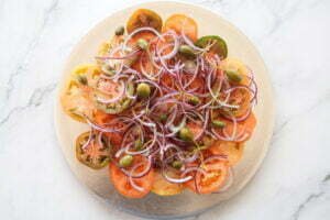 tomato slices, red onion, capers sit on a servingplatter