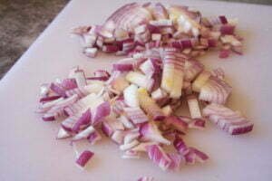 Diced red onion sits on a white plastic chopping board.