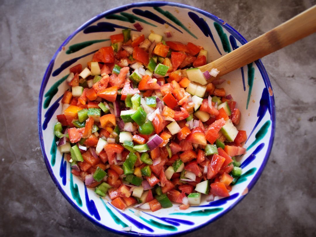 Some Pipirrana Spanish salad sits in a colorful bowl on a grey slate counter.