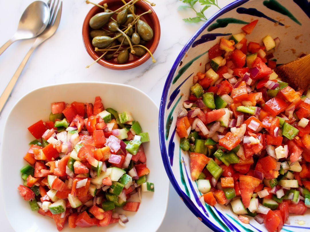 A large colorful bowl of Pipirrana Spanish Salad sits waiting to be served to a. small white bowl. 