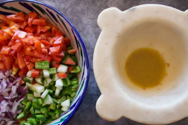 A large colorful bowl full of salad ingredients suts beside a mortar with some salad dressing