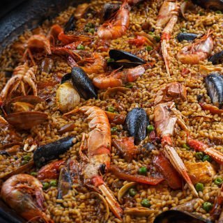 A large seafood paella sits with large shrimp, mussels, and other seafood scattered on top.