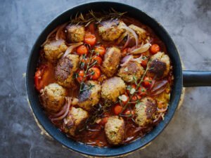 A large pan of vegetarian meatballs sits garnished with cherry tomatoes and thin slices of red onion