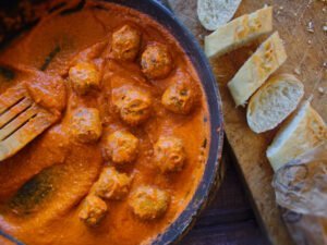 A alrge frying pan sits cooking some albondigas and sofrito saucce beside a few slices of sliced white bread.